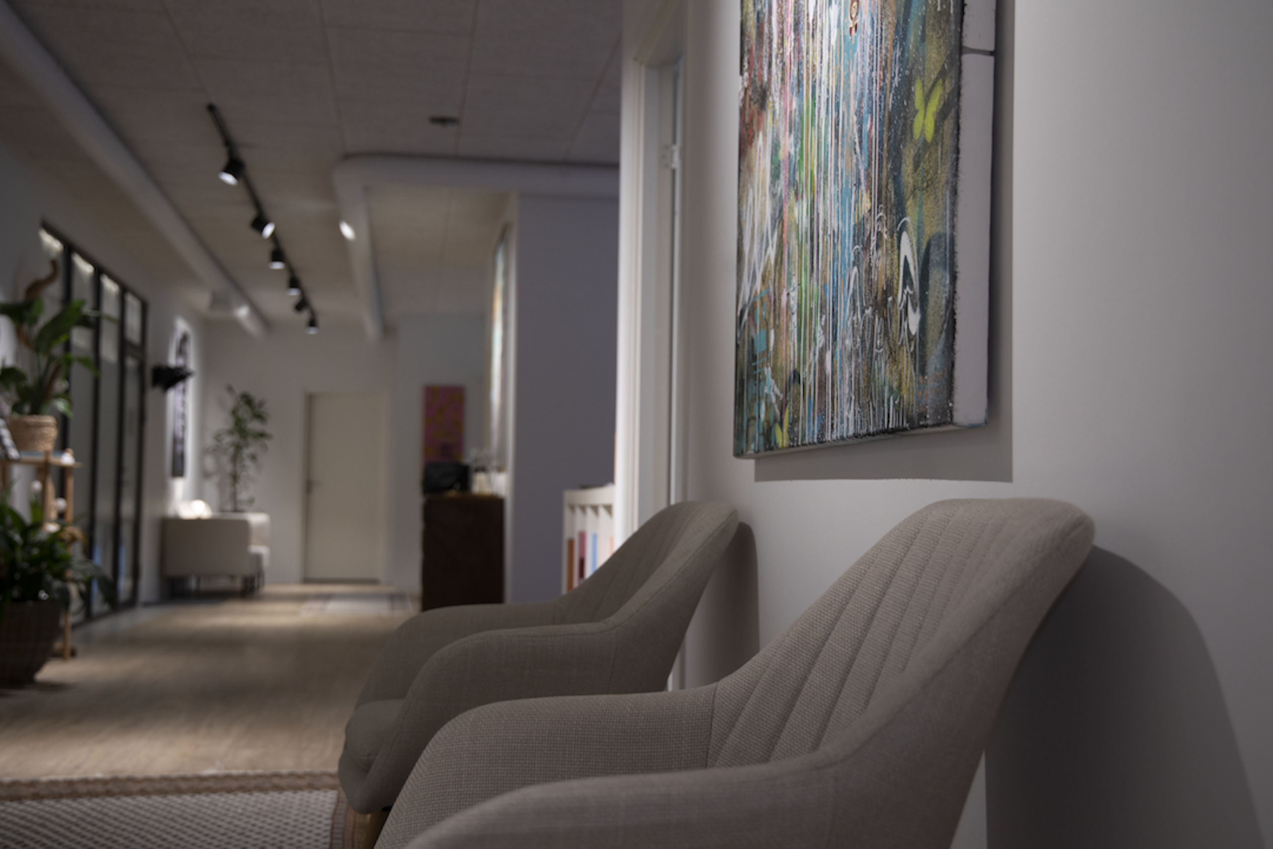 Contemporary gallery interior with a large colorful wall painting and beige upholstered chairs along a hallway.