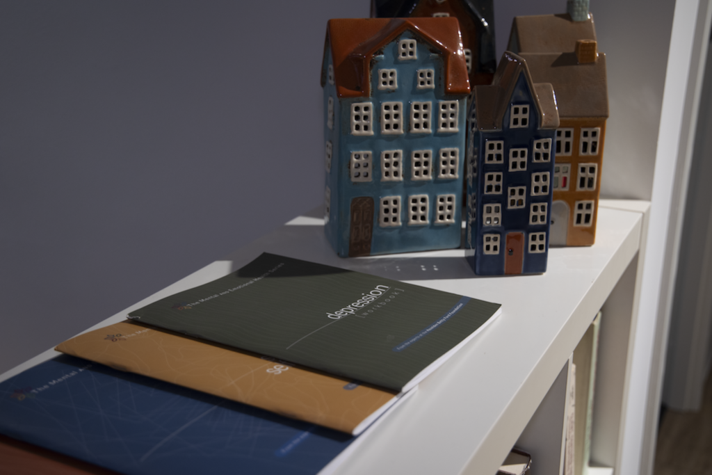 Decorative ceramic houses in blue, teal, and orange on a white shelf with magazines in the foreground.